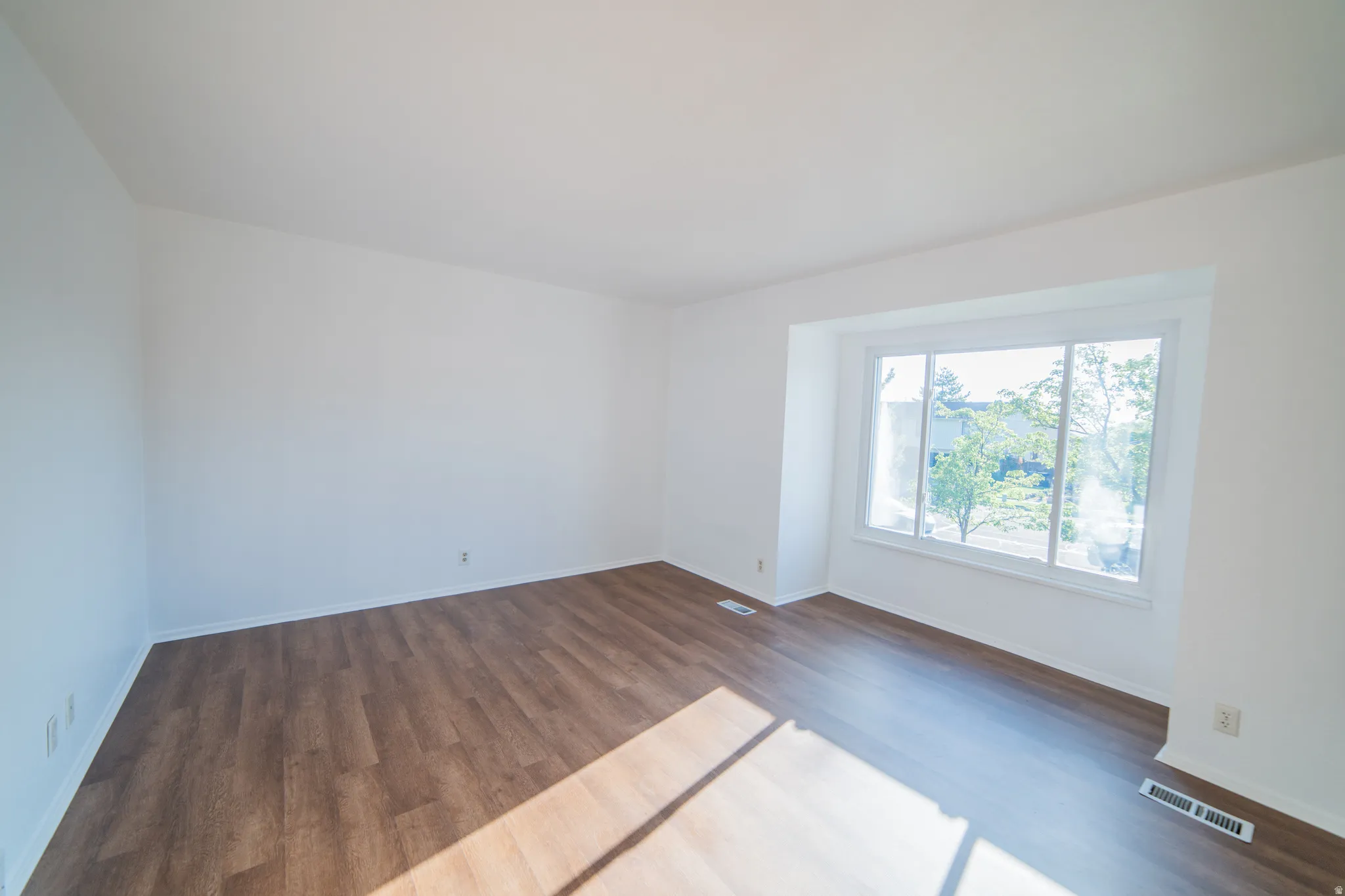 Spacious room featuring wood-finish flooring, white walls, and a large bay window