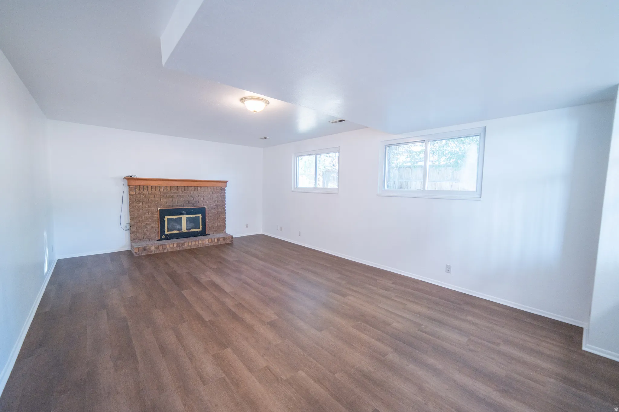 Spacious interior with wood-finish flooring, a brick fireplace with a wood mantle, and multiple windows
