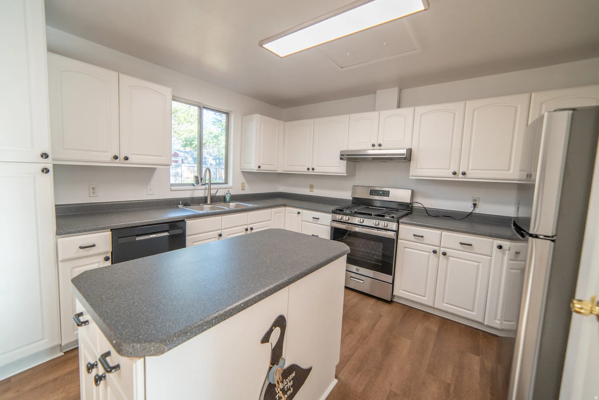 White cabinetry with dark hardware, a central island, stainless steel appliances, and wood-finish flooring