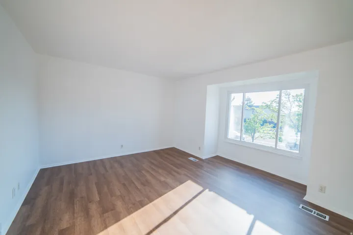 Spacious room featuring wood-finish flooring, white walls, and a large bay window