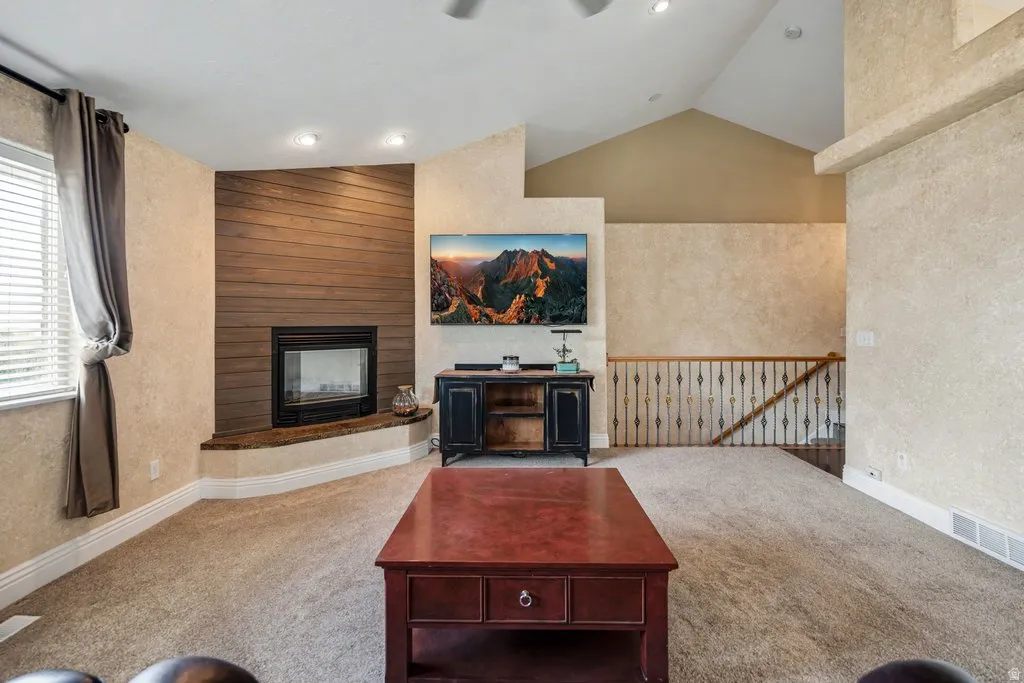 Vaulted ceiling with recessed lighting, corner fireplace with wood-finish accent wall, and wrought iron railing