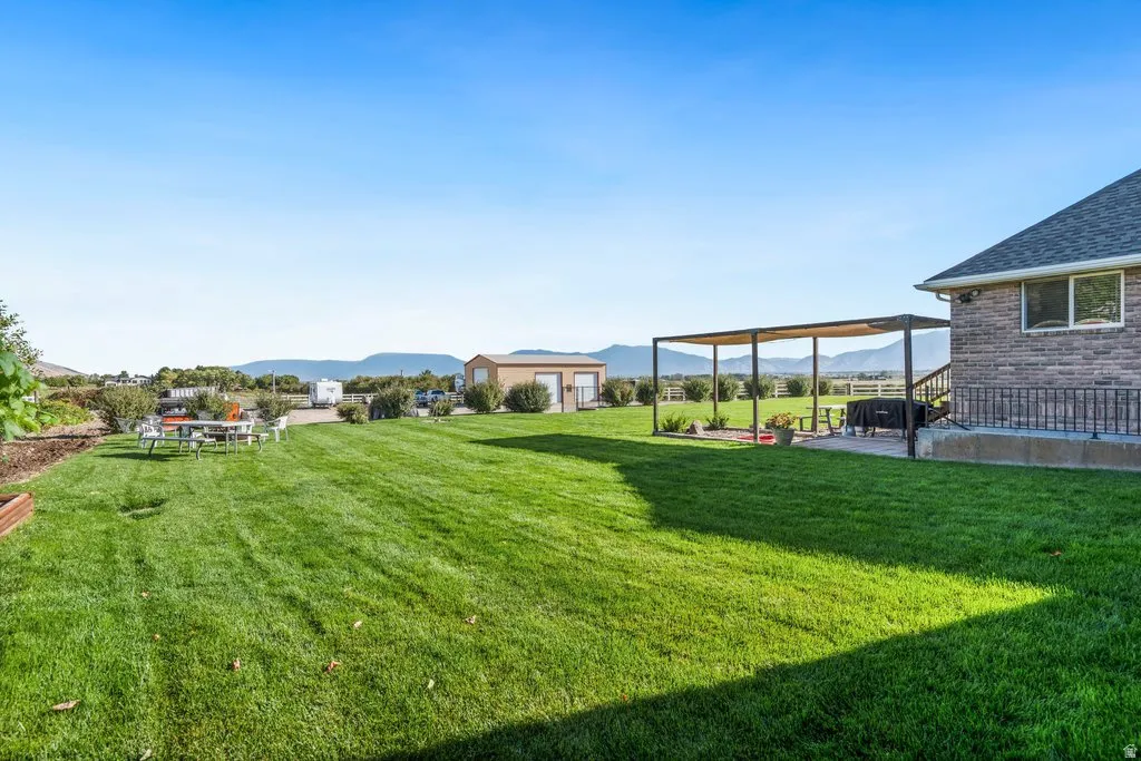Well manicured gorgeous and healthy lawn with mountain scenery, a stone-clad exterior, and a patio with an attached pergola