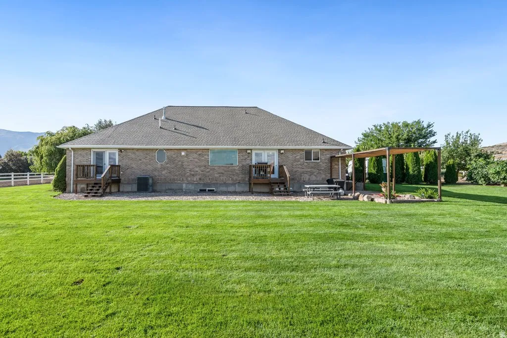 Expansive lawn area with a pergola, two wooden decks, and a brick exterior with a shingle roof