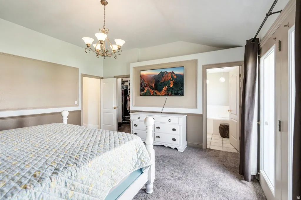 Primary bedroom with vaulted ceiling with decorative chandelier, carpeted flooring, built-in wall paneling detail, and double French doors