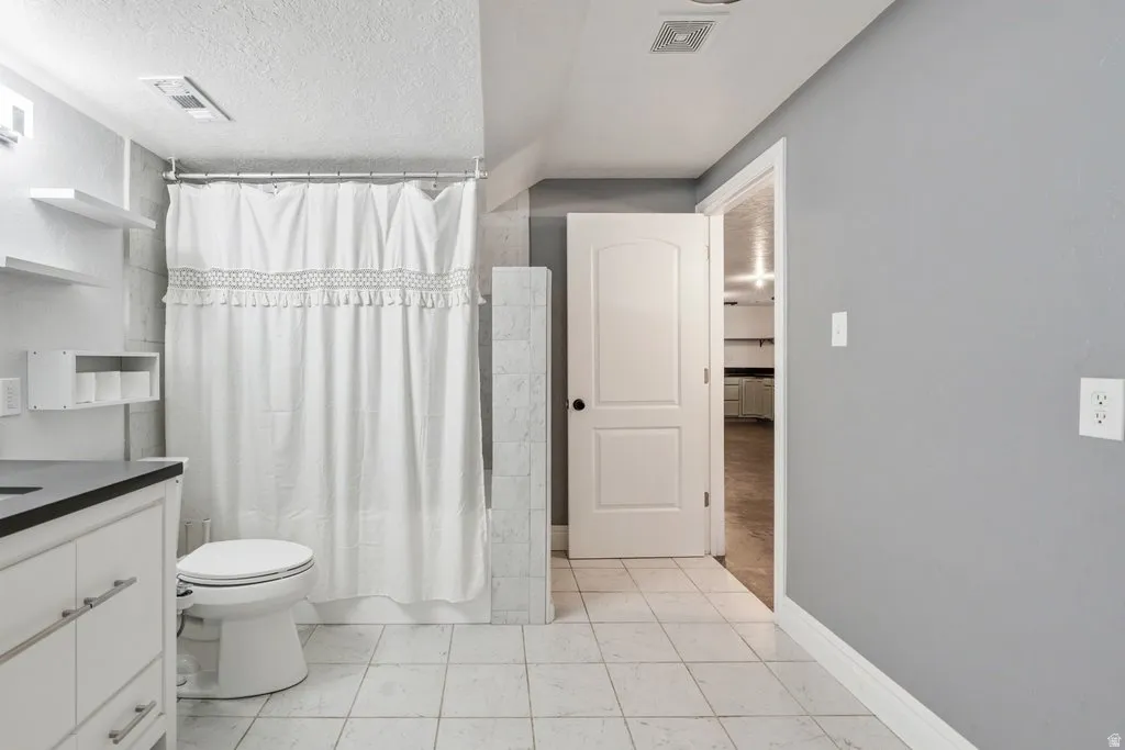 Bathroom featuring white tile flooring, a white vanity with black countertop, and a white toilet