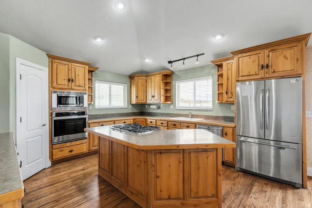 Kitchen featuring wood-finish flooring, recessed lighting, wood cabinetry, a center island with a cooktop, and stainless-steel appliances