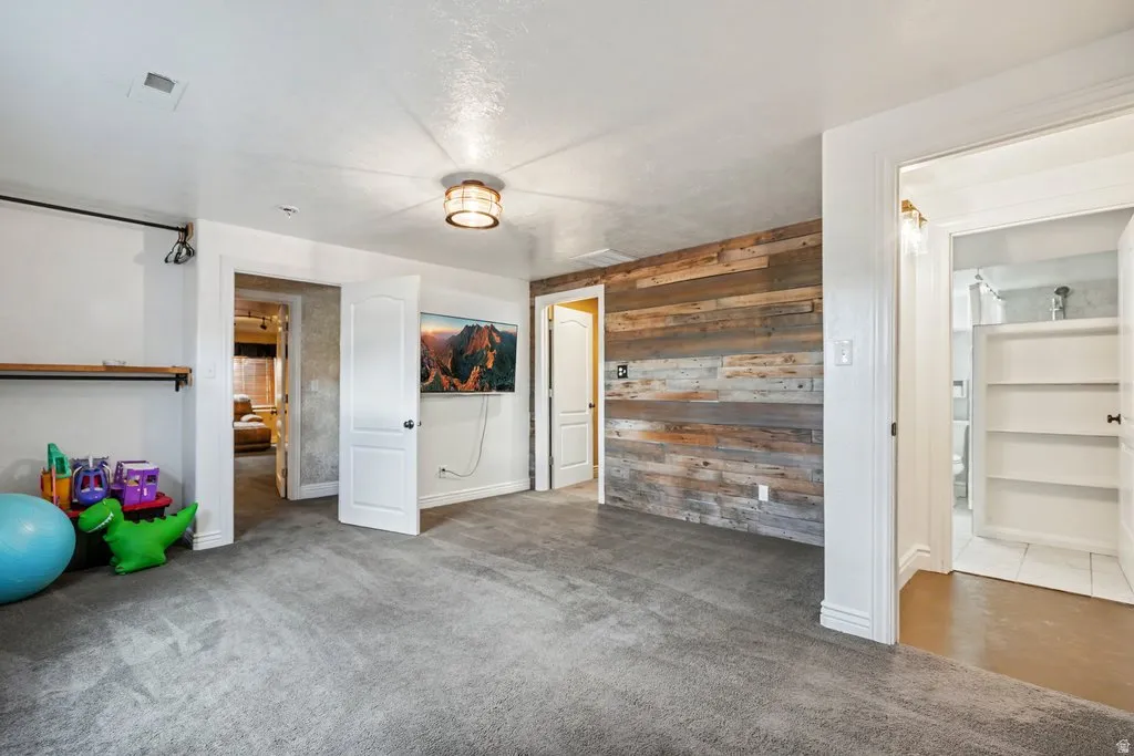 Carpeted room featuring a wood-panel accent wall, recessed lighting, and a built-in wall shelf