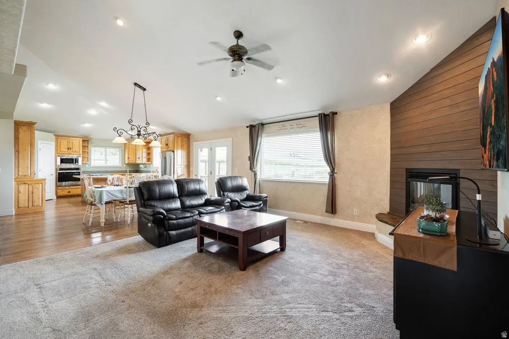 Vaulted ceilings with recessed lighting, wood-finish flooring, wood cabinetry with built-in appliances, a fireplace with a wood-paneled accent wall, and French doors