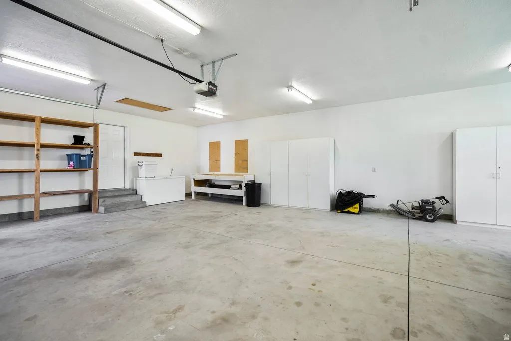 Spacious garage with concrete flooring, built-in wooden shelving, extensive white cabinetry, and overhead fluorescent lighting