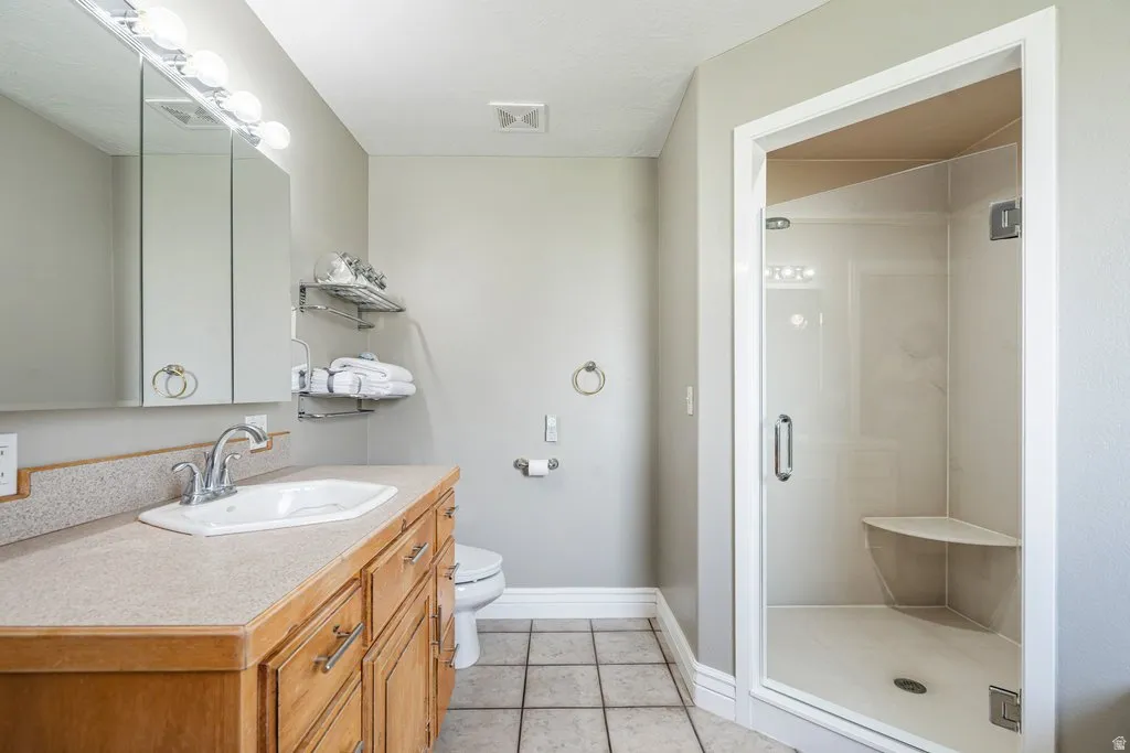 Spacious bathroom featuring a wood-finish vanity with an integrated sink, a glass-enclosed shower with a built-in bench, and square floor tiles