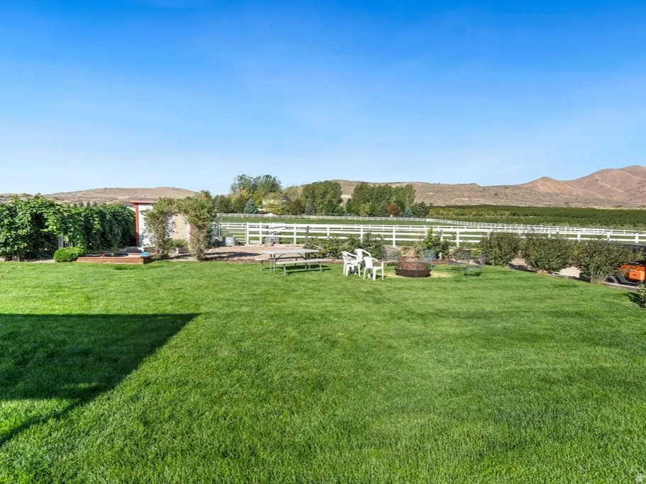 Expansive lawn area with a white fence perimeter, mature landscaping, and distant mountain scenery