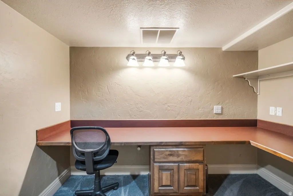 Built-in L-shaped desk with rich wood-finish countertop, integrated wood cabinetry, and overhead task lighting