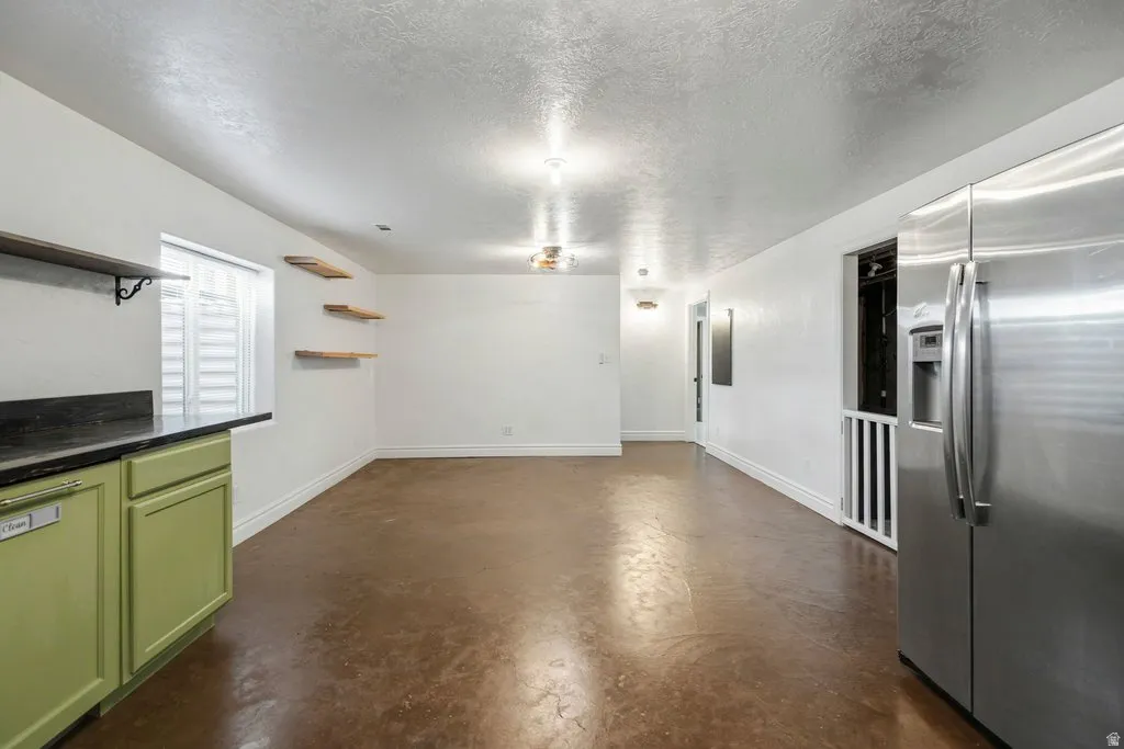 Kitchenette with green cabinetry, dark countertop, and stainless steel refrigerator with epoxy painted floor.