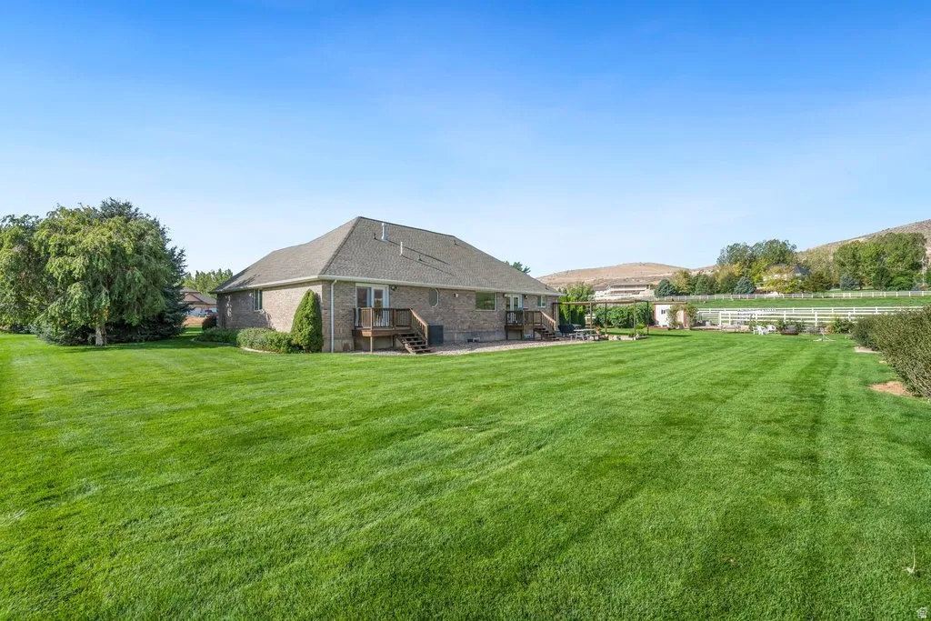 Expansive lawn, brick exterior, multi-level wood deck, mature trees, and white perimeter fencing
