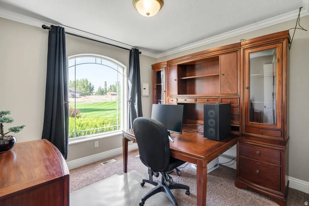 Arched window providing ample natural light, crown molding, built-in wood cabinetry, wood-finish desk, and carpeted flooring