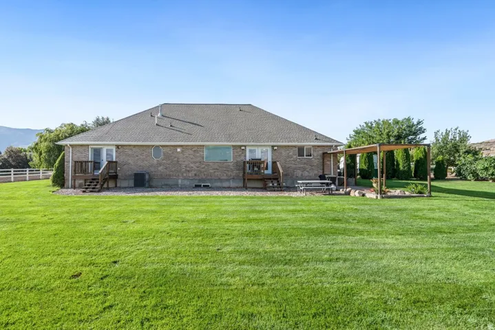 Expansive lawn area with a pergola, two wooden decks, and a brick exterior with a shingle roof