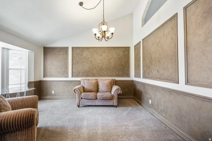 Vaulted ceiling, decorative wall paneling, chandelier lighting, bay window, and carpeting
