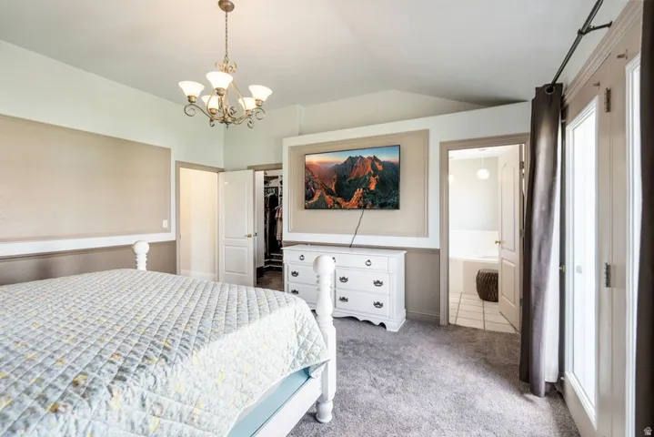 Primary bedroom with vaulted ceiling with decorative chandelier, carpeted flooring, built-in wall paneling detail, and double French doors