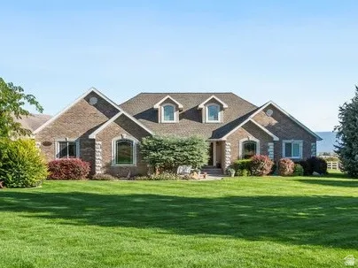 Expansive manicured lawn with mature trees, stone and brick exterior, and a dormered roofline
