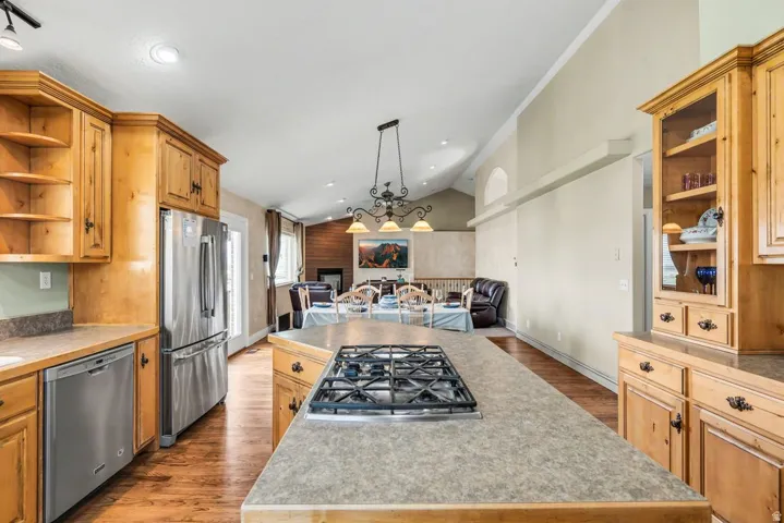 Kitchen featuring wood cabinetry, stainless steel appliances, an island with a built-in gas range, and wood-finish flooring