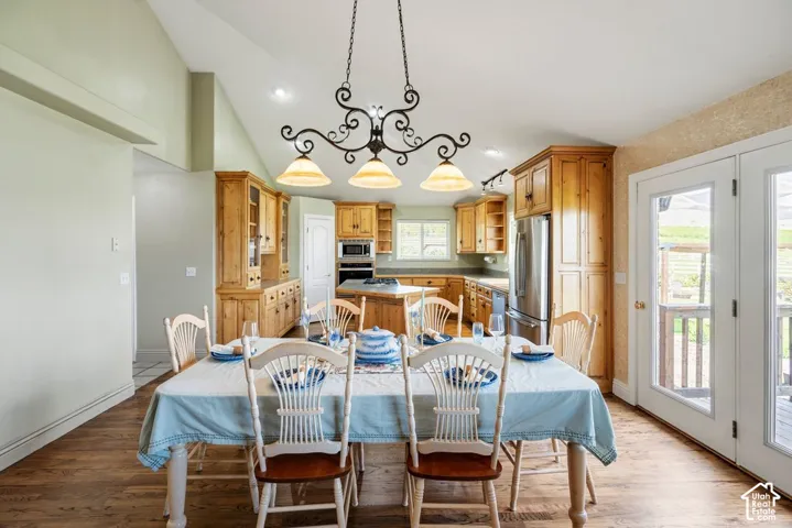 Kitchen and dining area featuring vaulted ceilings, wood-finish flooring, custom wood cabinetry, stainless steel appliances, and French doors
