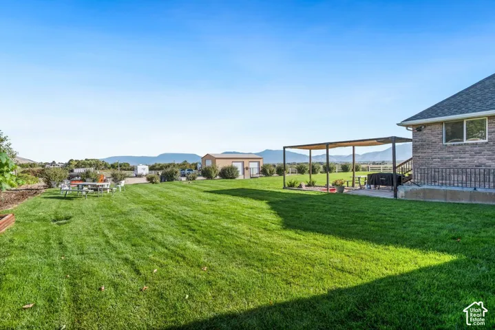 Well manicured gorgeous and healthy lawn with mountain scenery, a stone-clad exterior, and a patio with an attached pergola