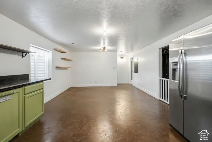 Kitchenette with green cabinetry, dark countertop, and stainless steel refrigerator with epoxy painted floor.