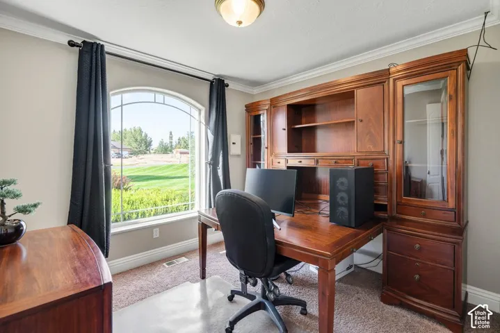 Arched window providing ample natural light, crown molding, built-in wood cabinetry, wood-finish desk, and carpeted flooring