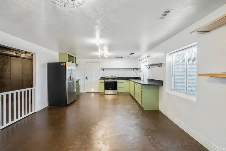 L-shaped kitchen with green cabinetry, dark countertops, stainless steel appliances.