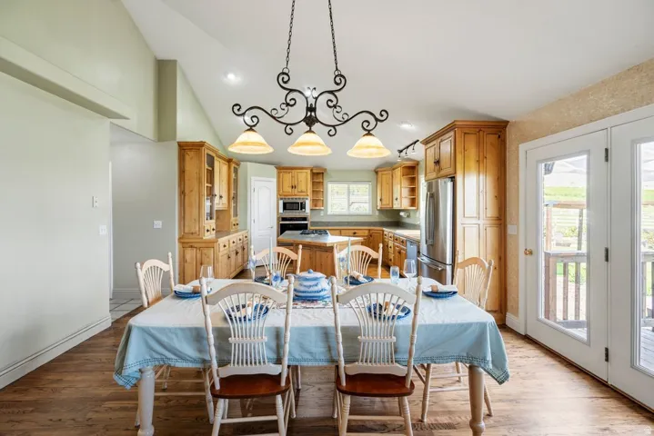 Kitchen and dining area featuring vaulted ceilings, wood-finish flooring, custom wood cabinetry, stainless steel appliances, and French doors