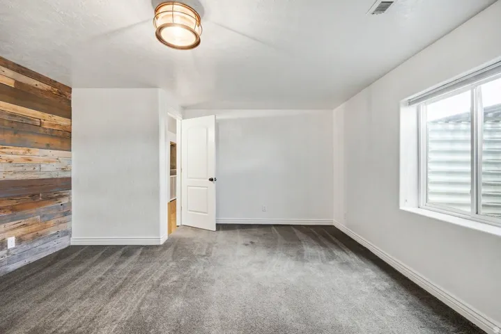 Textured wood accent wall, neutral carpeting, white interior paint, white trim, and a contemporary ceiling light fixture
