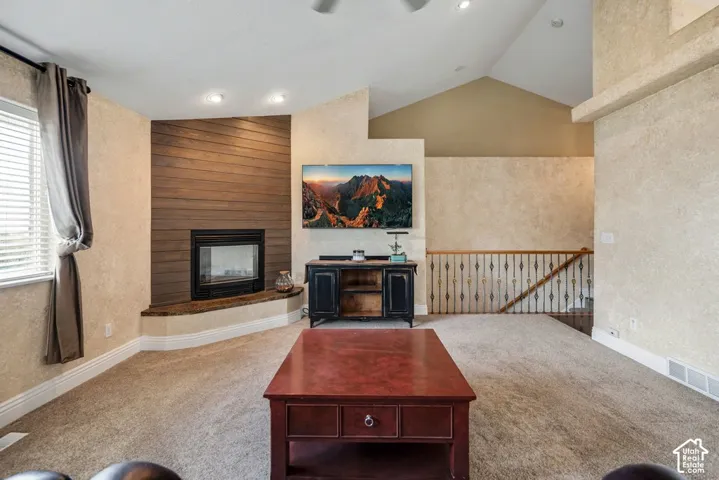 Vaulted ceiling with recessed lighting, corner fireplace with wood-finish accent wall, and wrought iron railing