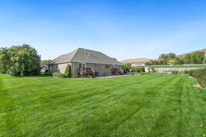 Expansive lawn, brick exterior, multi-level wood deck, mature trees, and white perimeter fencing