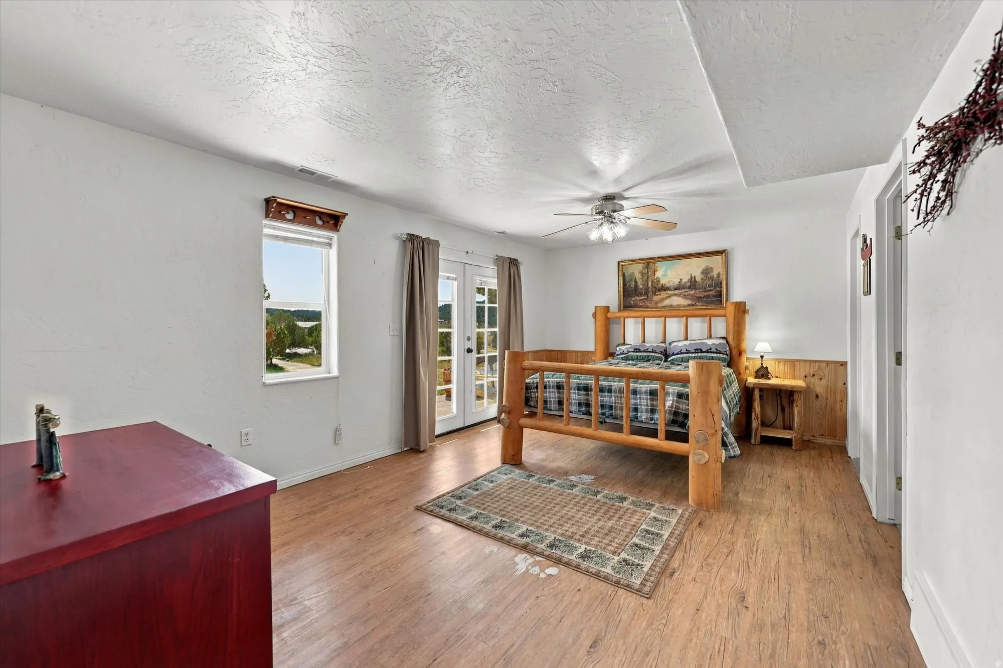 Wood-finish flooring, ceiling fan with light fixture, natural wood wainscoting, and double French doors