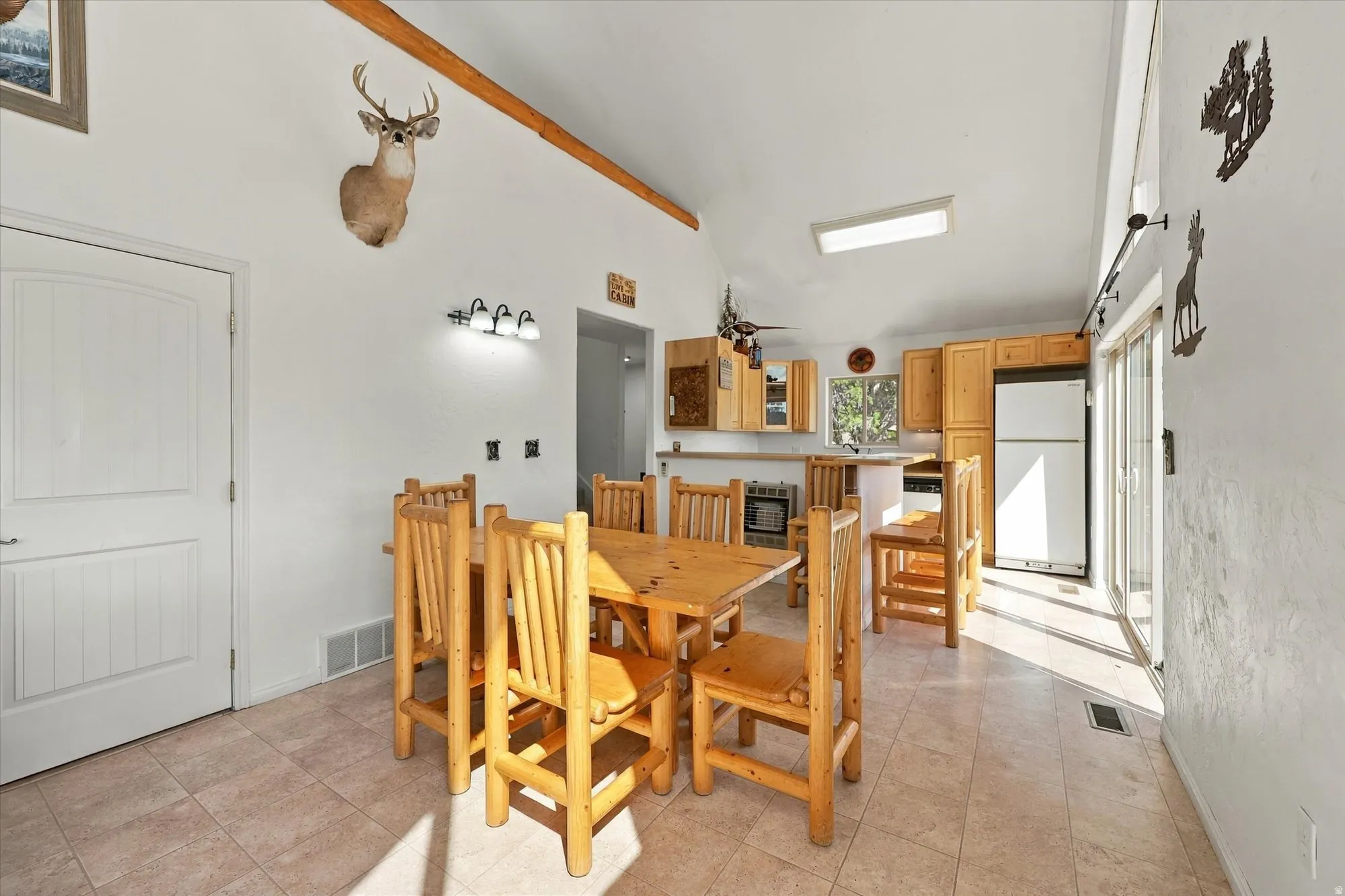 Vaulted ceilings with exposed wood beams, tile flooring, sliding glass door, and a kitchen featuring wood cabinetry