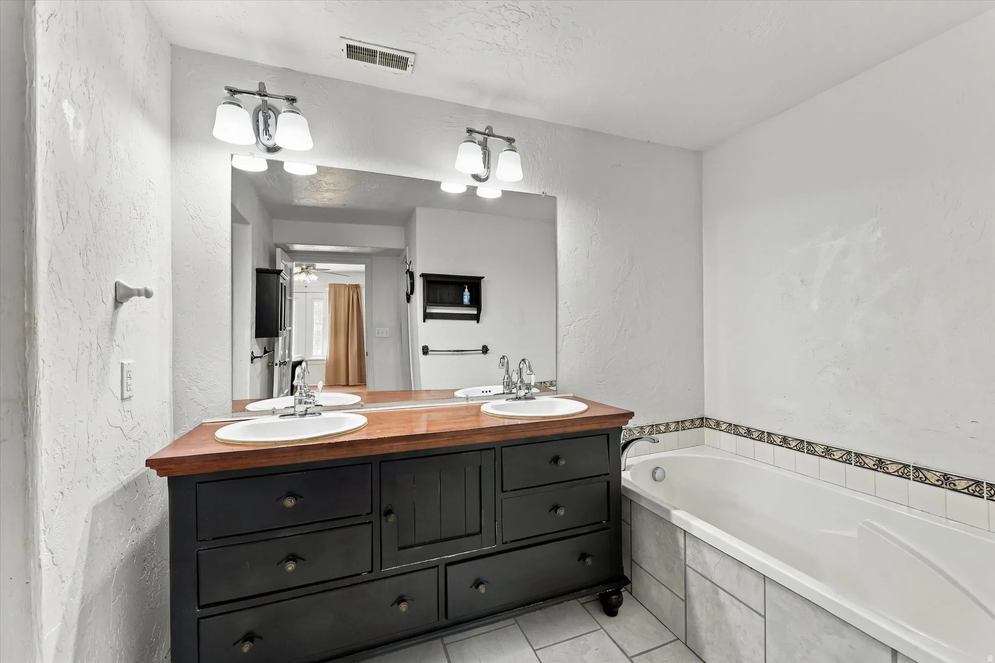 Double vanity with wood-finish countertop, two undermount sinks, and wall-mounted light fixtures