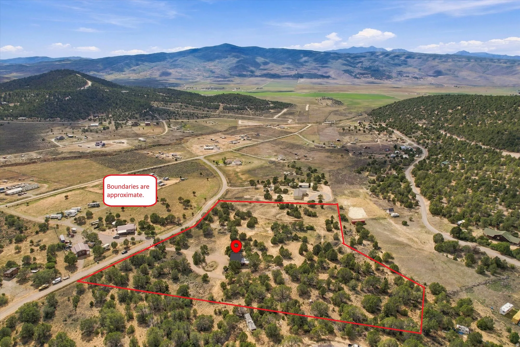Expansive property with a verdant landscape and mature trees, featuring a marked boundary, a visible structure, and mountainous terrain in the background