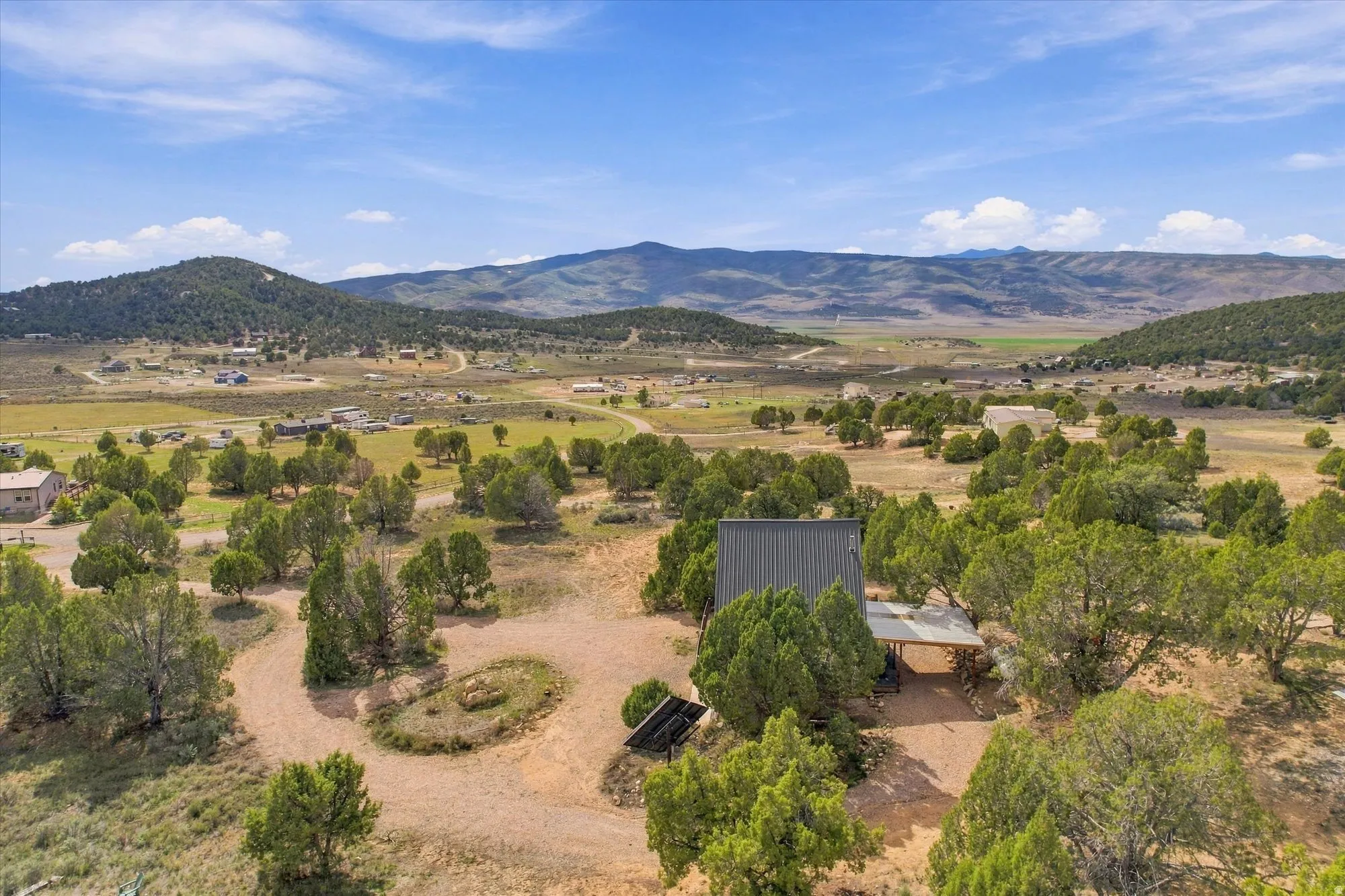 Expansive rural property featuring a contemporary home with a metal roof, surrounded by mature trees and natural landscaping