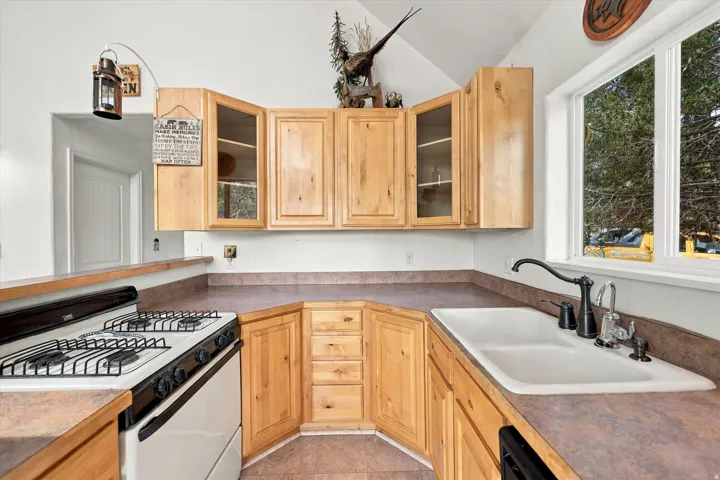 Kitchen featuring wood cabinetry, warm-toned countertops, a built-in gas range, a double basin sink with a gooseneck faucet, and a large window
