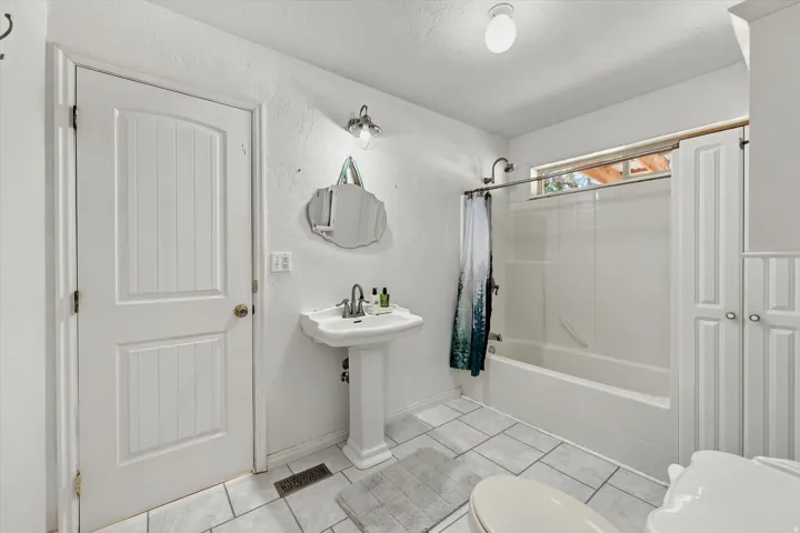 Pedestal sink with polished chrome faucet, built-in bathtub with shower, and tiled flooring