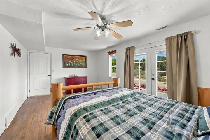Wood-finish flooring, white paneled door, ceiling fan with light fixture, and double glass-paneled doors
