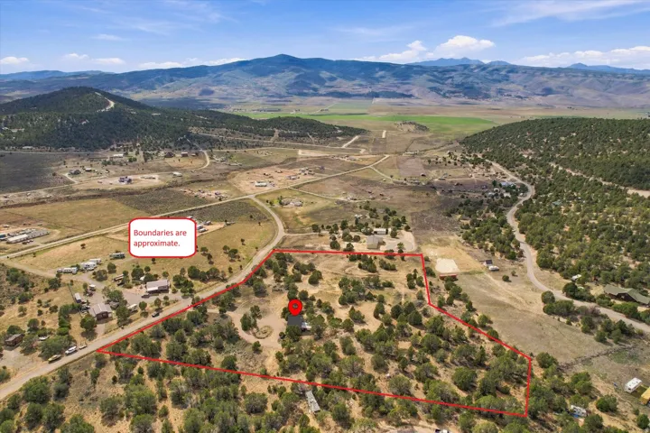 Expansive property with a verdant landscape and mature trees, featuring a marked boundary, a visible structure, and mountainous terrain in the background