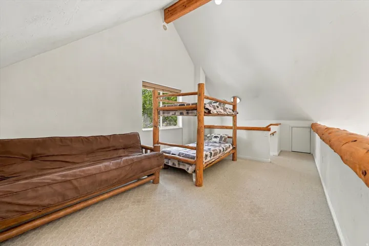 Vaulted ceiling with exposed wood beams, neutral carpeting, and a window with natural light