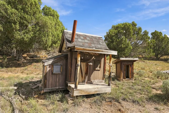 Wood-sided structure with a covered porch, shingle roofing, and a metal chimney