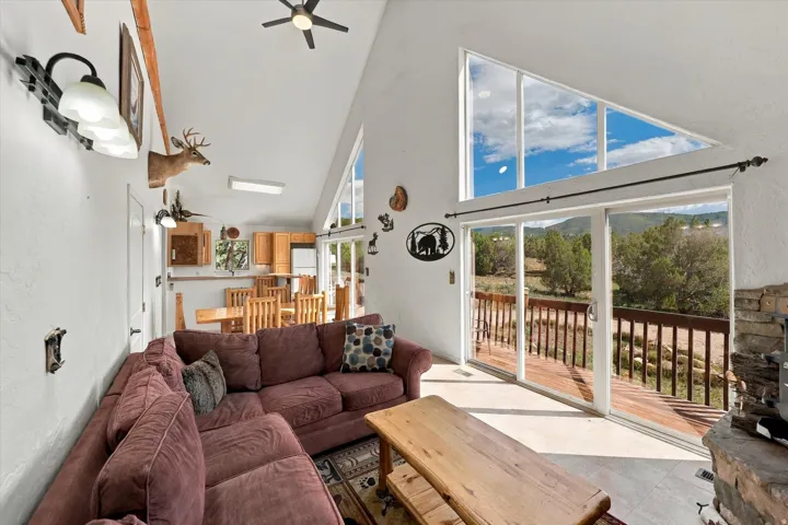 Vaulted ceilings with exposed wood beams, expansive floor-to-ceiling windows, sliding glass door access to an outdoor deck, and an open-concept kitchen with wood cabinetry