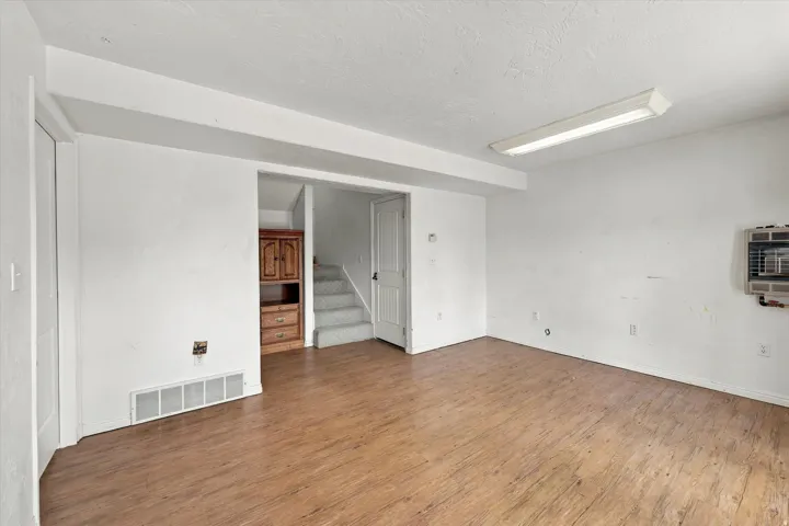 Spacious room featuring wood-finish flooring, white walls, and a built-in wall heater