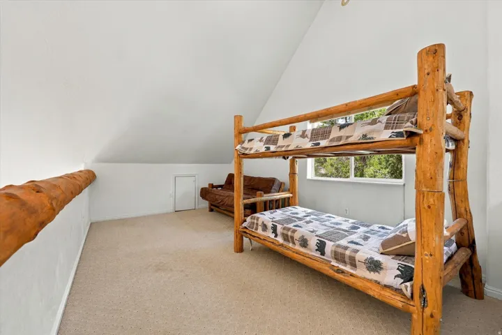 Carpeted room with a pitched ceiling, a wood-finish railing, and a window providing natural light