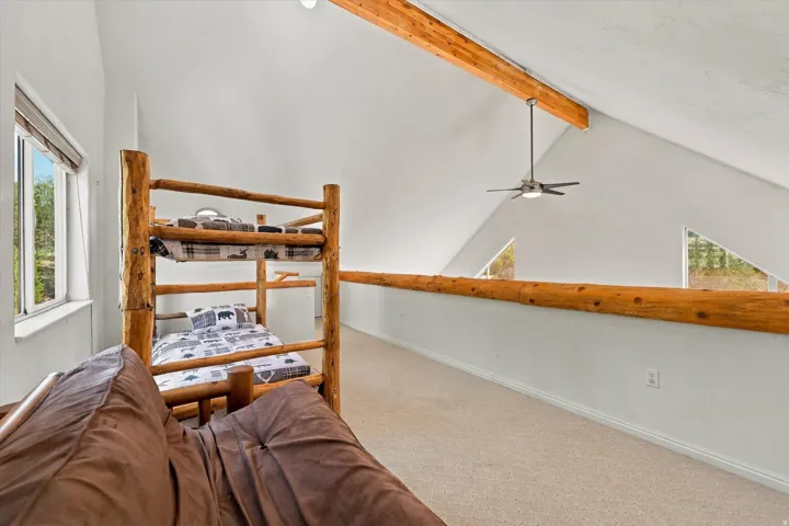 Vaulted ceiling with exposed wood beams and ceiling fan, white walls, and light-colored carpeting