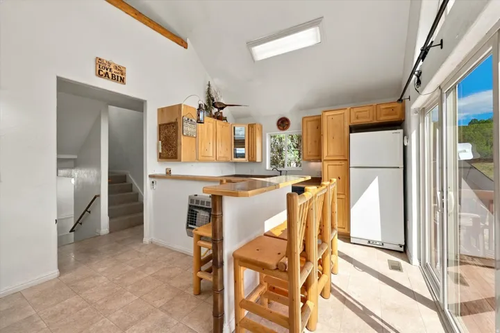 Kitchen featuring wood cabinetry, a breakfast bar with seating, tile flooring, and vaulted ceilings with an exposed beam