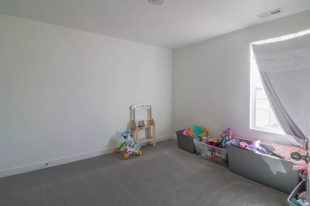 Recessed ceiling lighting, white painted walls, gray carpet flooring, and a single window with a white frame